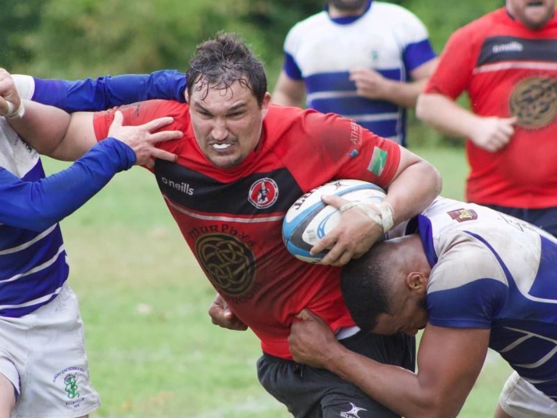 Man being tackled playing rugby and holding off player with hand to the face